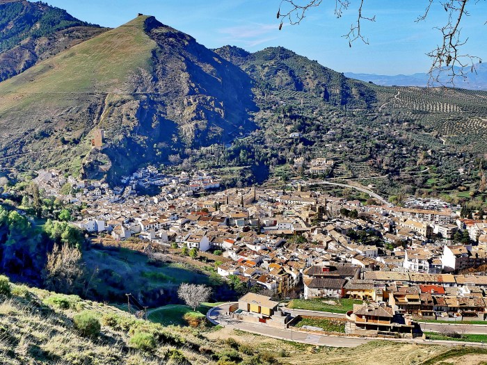 Die Stadt Cazorla am Hang, eingebettet am Fuße grüner und felsiger Berge unter einem klaren blauen Himmel.